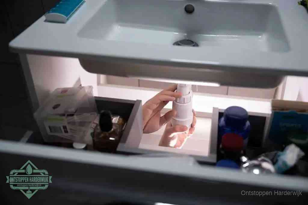 Een pompfles met zeep boven een wastafel, de heet water en afwasmiddel-methode om een vetprop in de afvoer los te maken in Harderwijk