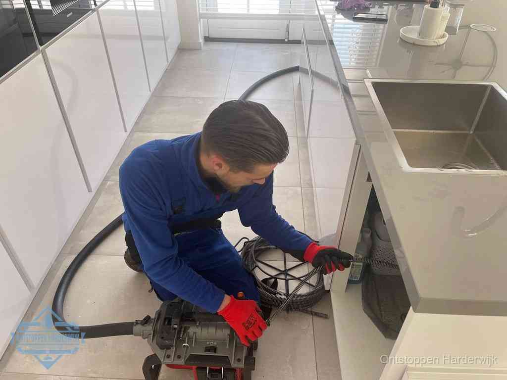 Een monteur ontstopt de keukenafvoer onder de spoelbak met een elektrische veermachine in Harderwijk