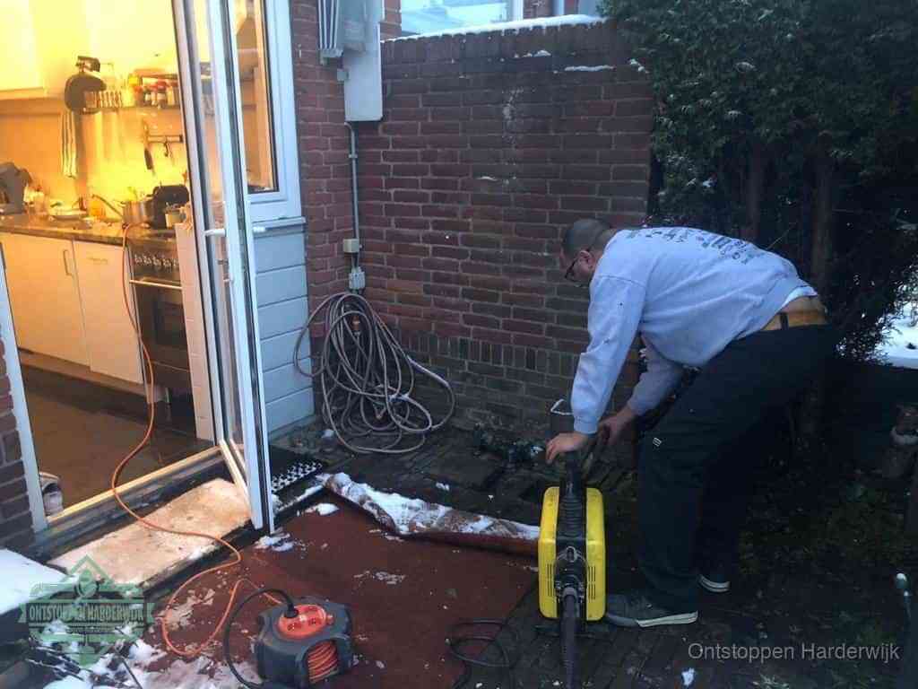 Een monteur werkt buiten bij een open riool-/grondput met een elektrische ontstoppingsmachine om een verborgen afvoerprobleem op te sporen in Harderwijk