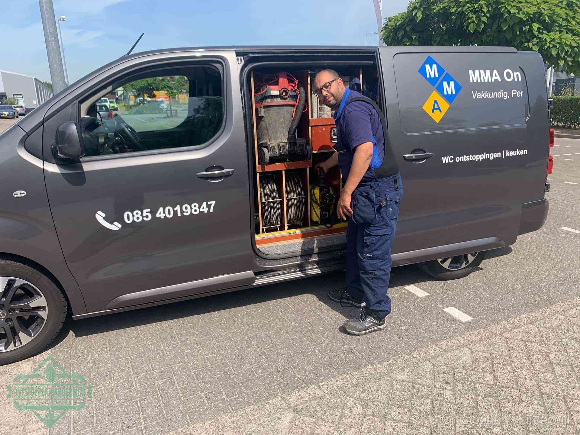 Een monteur bij de open schuifdeur van zijn bedrijfsbus op een parkeerplaats, klaar om de oorzaak van terugkerende afvoerverstoppingen aan te pakken in Harderwijk
