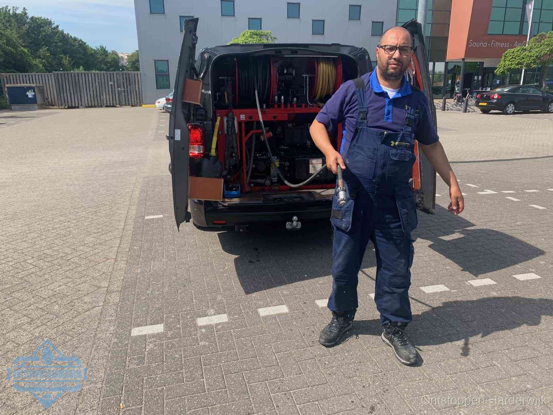 Een monteur bij zijn bestelbus met een hogedruk- en rioolreinigingsunit, klaar om de oorzaak van terugkerende wc-verstoppingen aan te pakken in Harderwijk