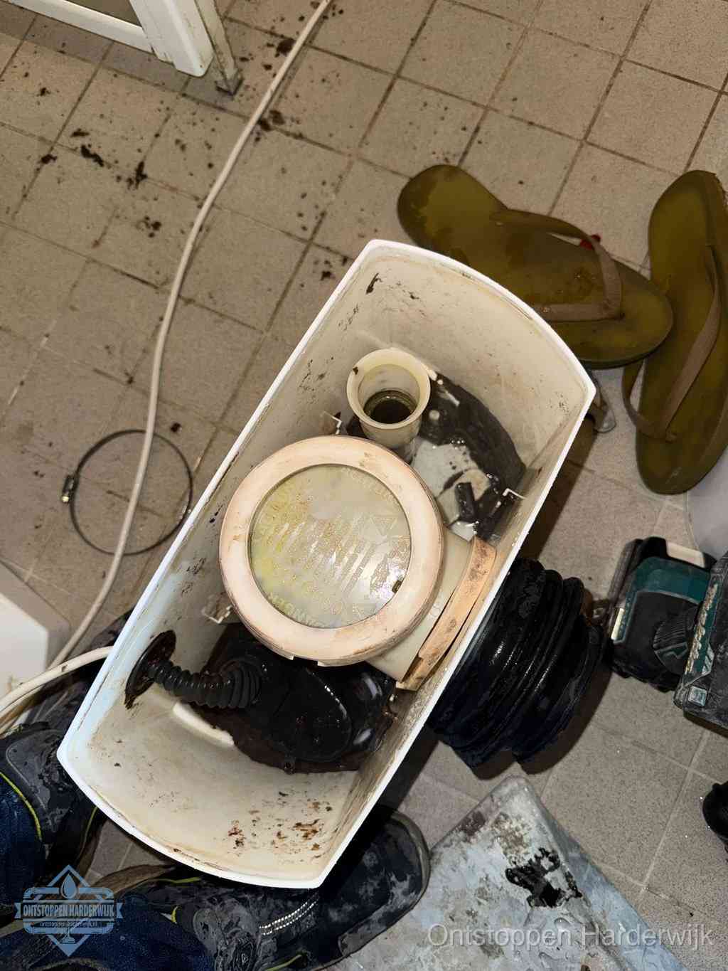 Een gedemonteerde toiletpot op de vloer met ontstoppingsveer en gereedschap ernaast, het verwijderen van een vastzittend voorwerp uit de wc in Harderwijk