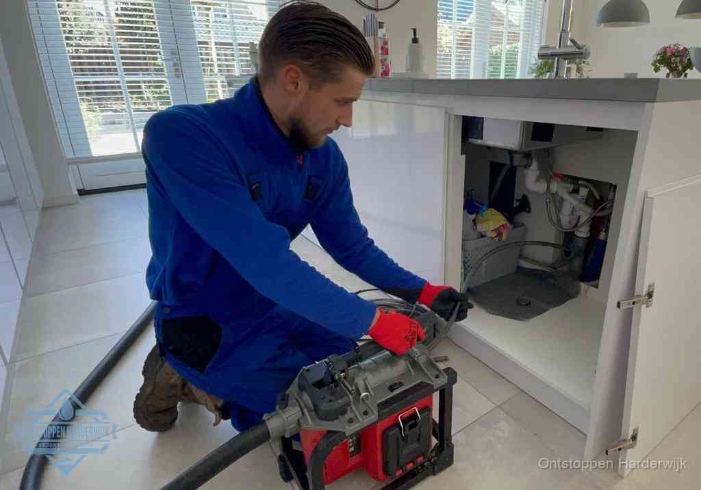 Een monteur voert een professionele elektrische ontstoppingsmachine in de afvoer onder de spoelbak tijdens het gootsteen ontstoppen in Harderwijk